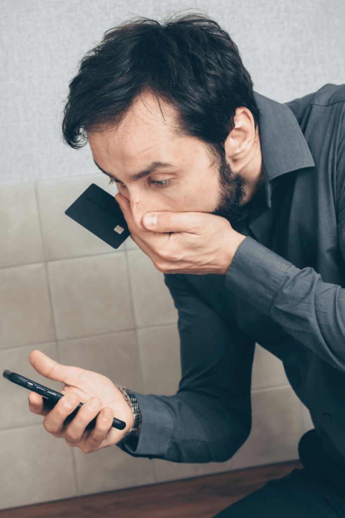 Man in shock as he looks at his debit card/credit card statement on his mobile phone.